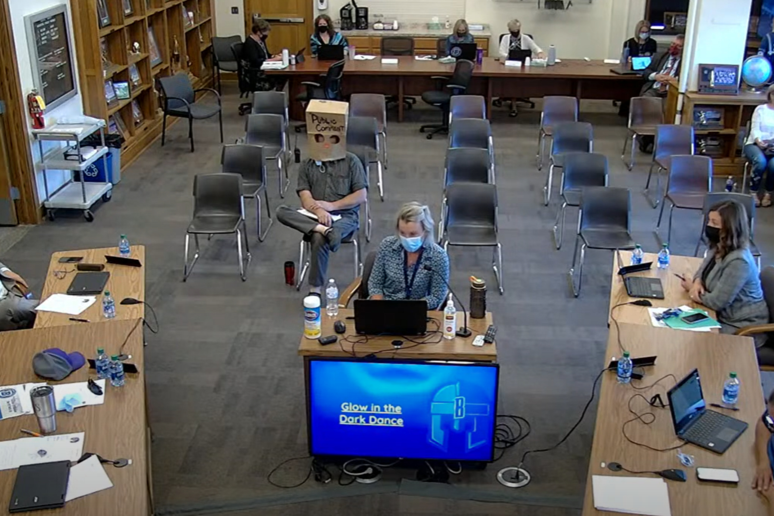 Principal Andrea Rusk speaks to her school board as a man wearing a grocery bag over his head looks on from the audience. (YouTube/ Brainerd Public Schools)