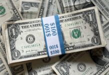 A stack of U.S. one-dollar bills bound in a $100 band with additional bills underneath.