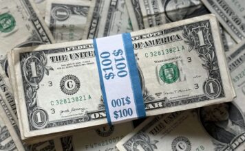A stack of U.S. one-dollar bills bound in a $100 band with additional bills underneath.
