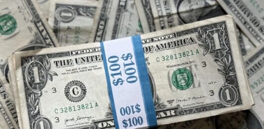 A stack of U.S. one-dollar bills bound in a $100 band with additional bills underneath.