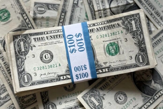 A stack of U.S. one-dollar bills bound in a $100 band with additional bills underneath.